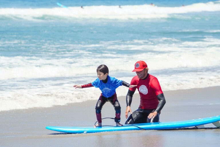 Professional surf coach teaching a student how to stand on a surfboard.