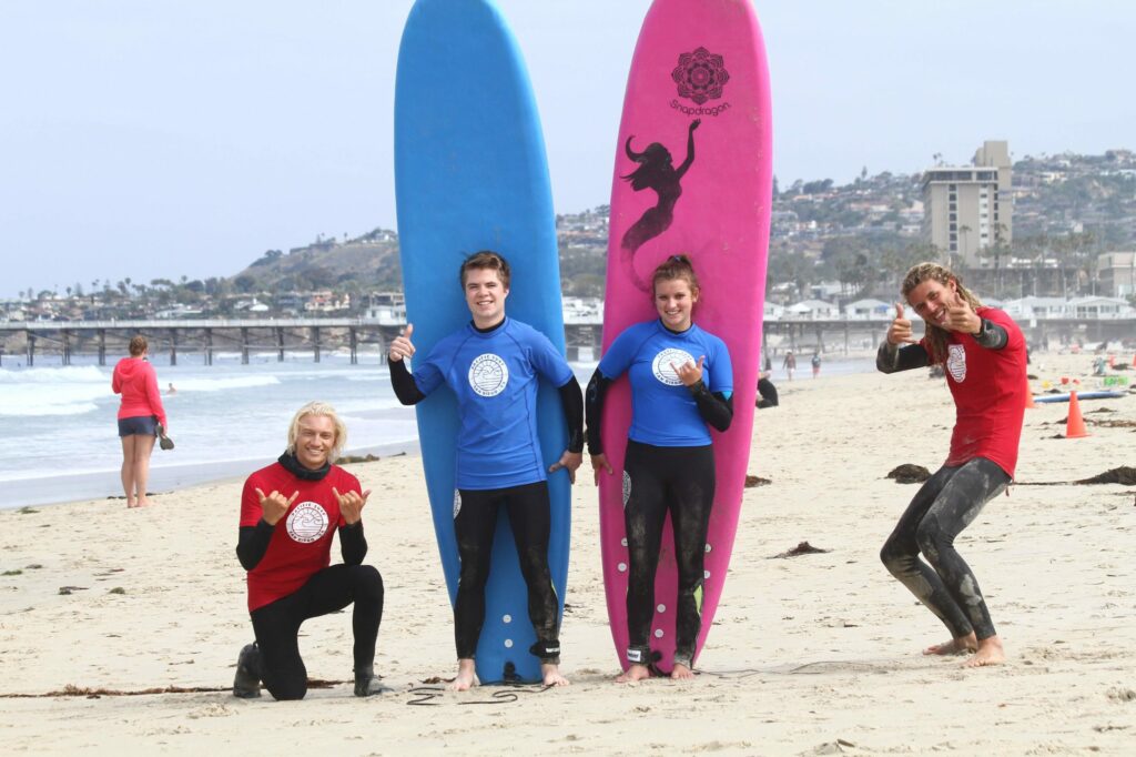 Surf instructors and their surf students posing for a picture on the beach after a successful surf lesson.
