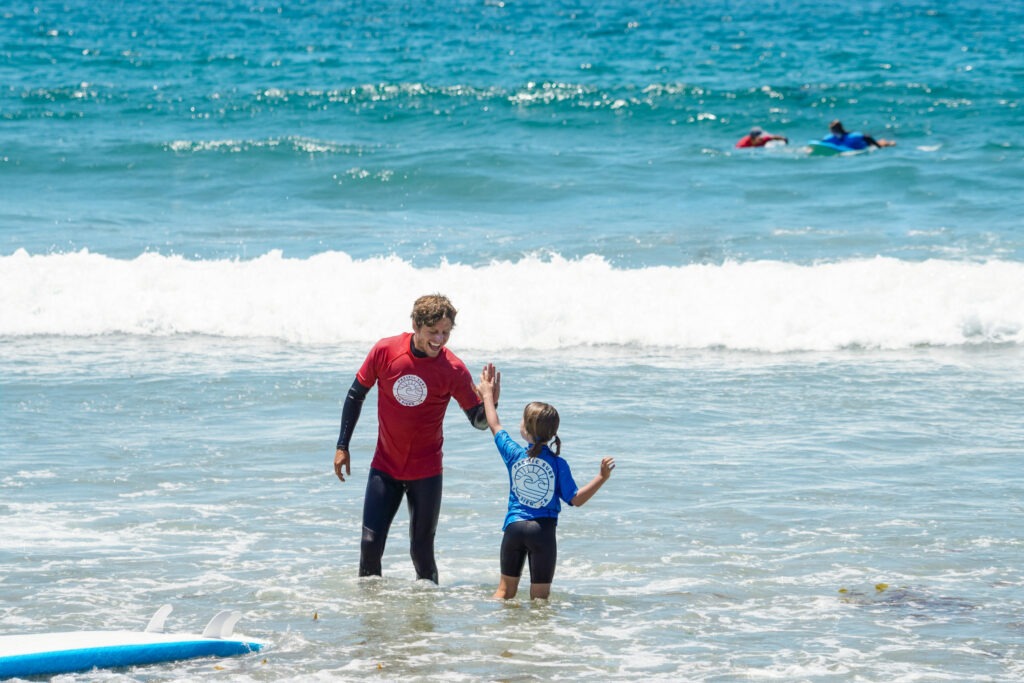 Surf instructor teaching a kid how to surf during a private surfing lesson in San Diego.