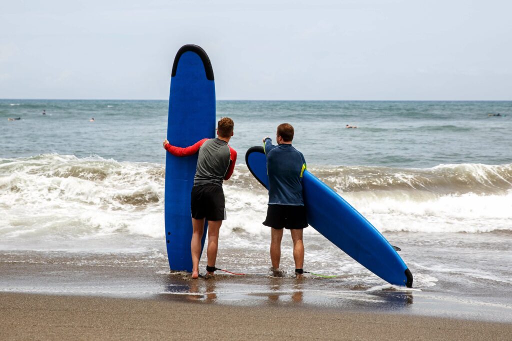 2 guys holding soft top surfboards looking into the ocean