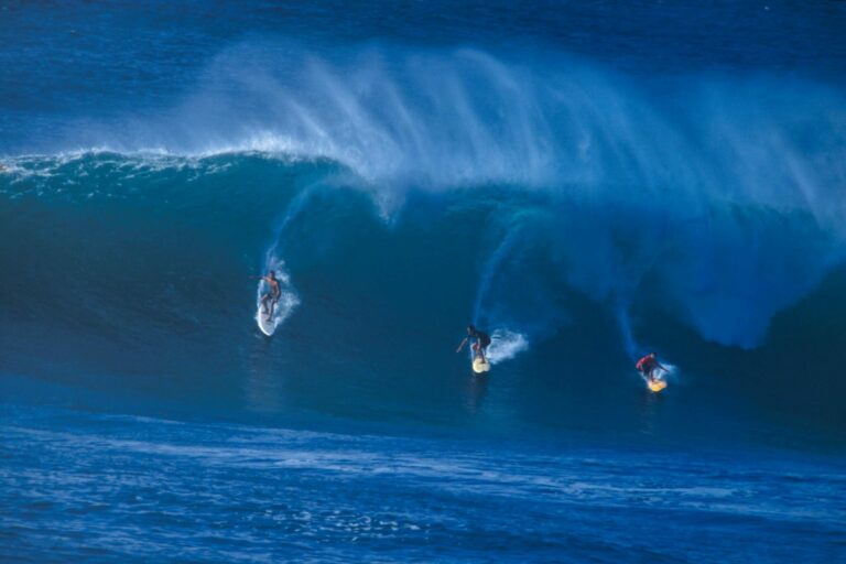 A group of 3 surfers riding down a large wave