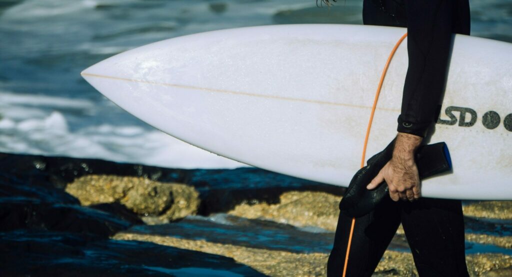 Man holding a hard top surfboard getting ready to go into the ocean