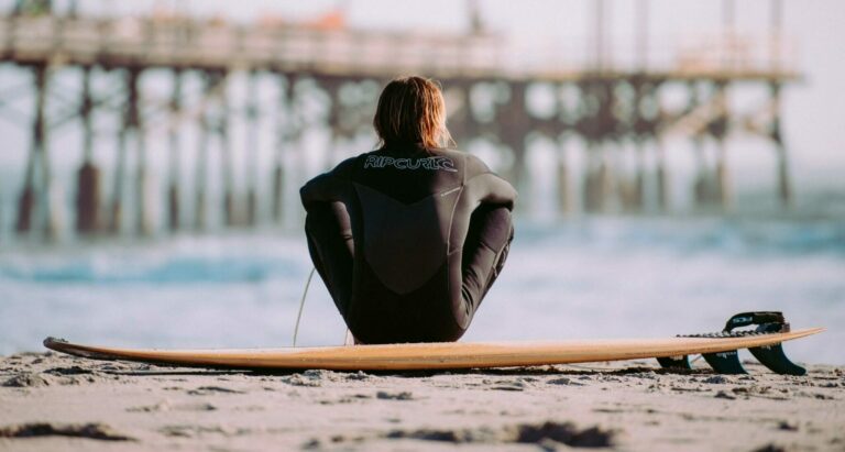 Beginner surfer sitting with his surfboard along the shoreline