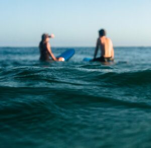 Two beginner surfers sitting on their surfboards in the ocean.