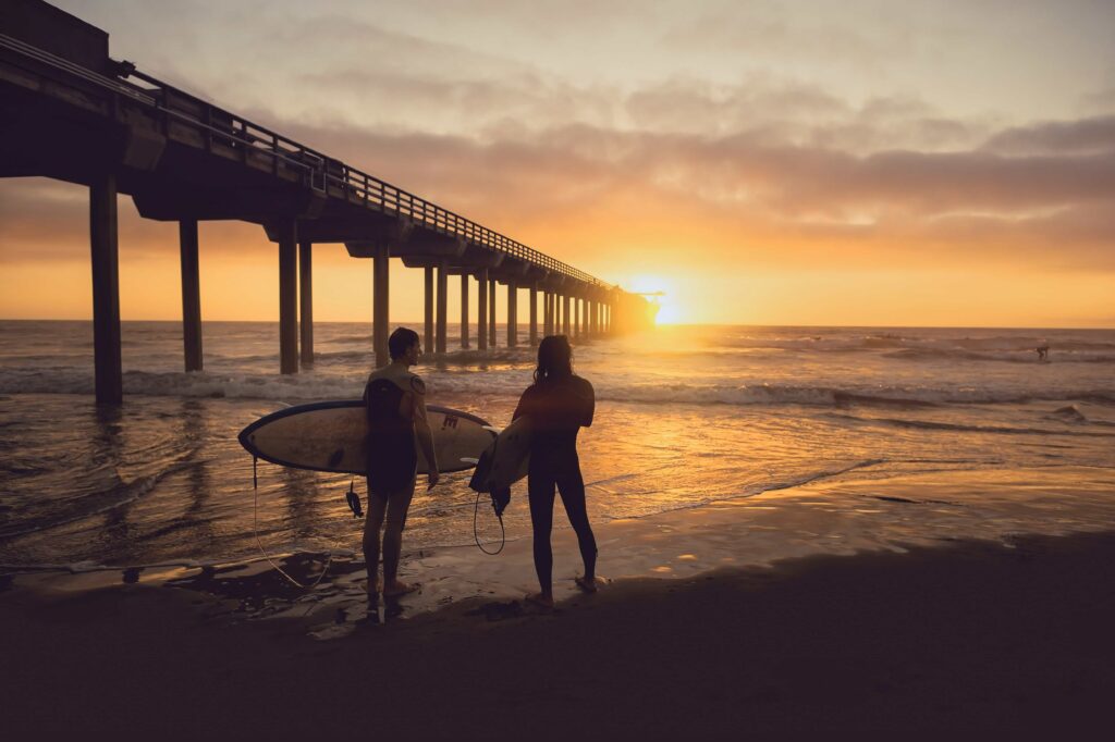 2 surfers standing at the shoreline with surfboards about to go into the ocean.