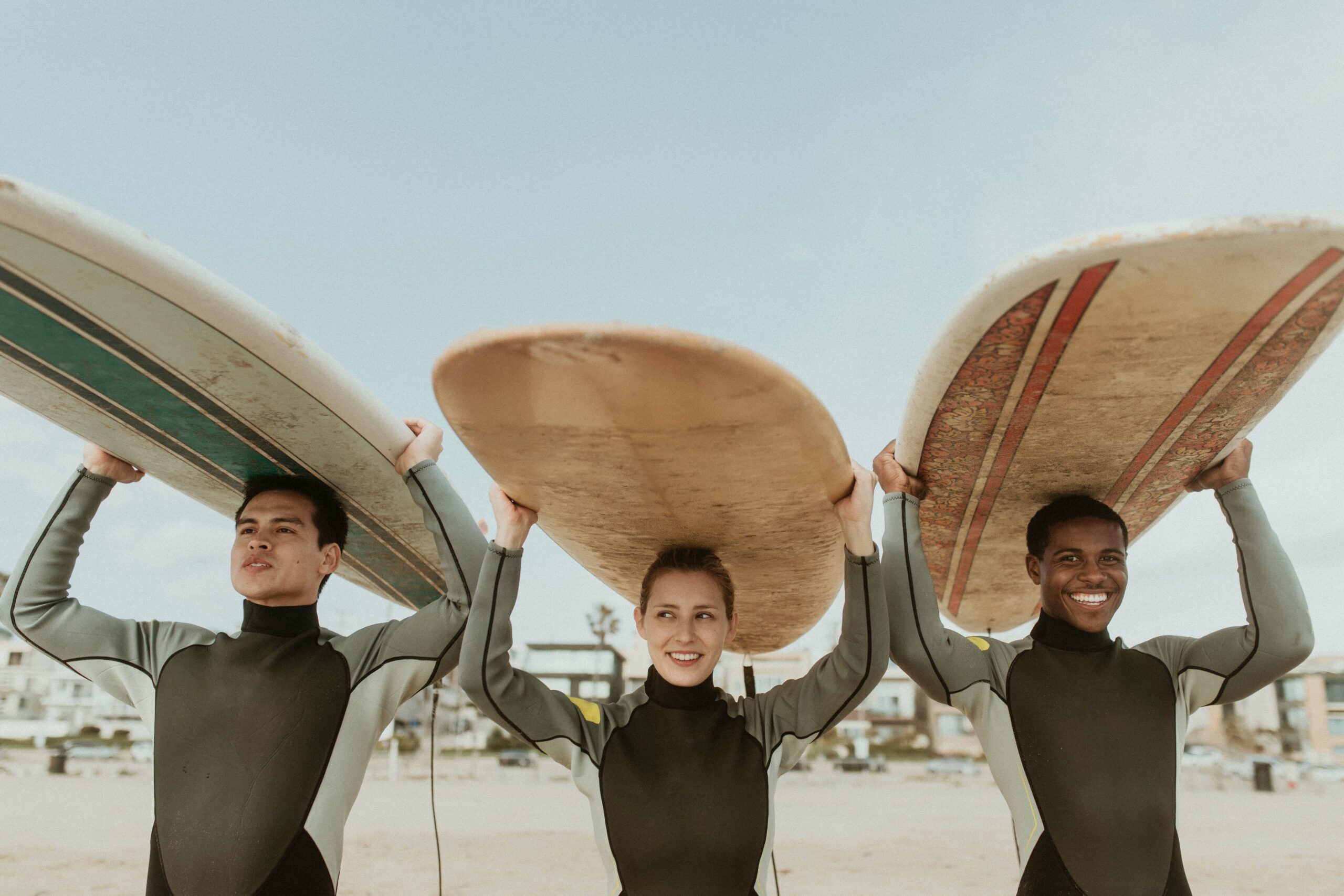 Group of 3 surfers holding different size surfboards above their heads.