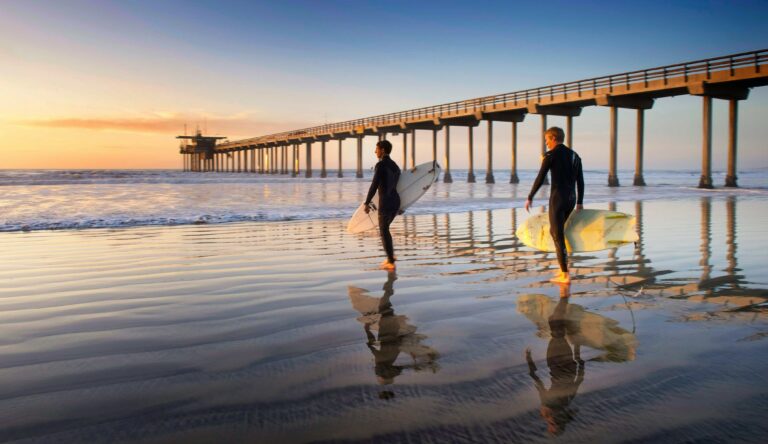 Two surfers going into the ocean with their surfboard during the best time to surf in San Diego.