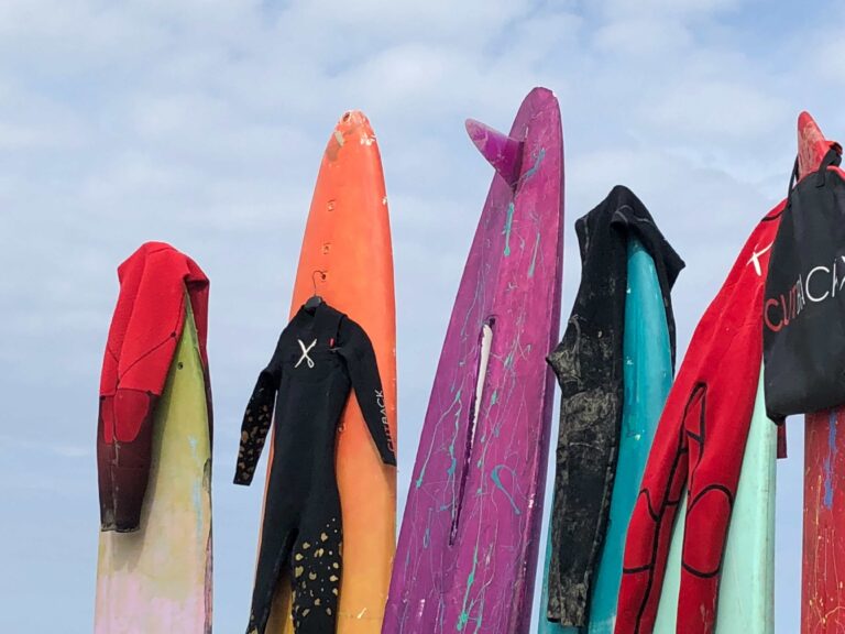 An assortment of wetsuits hanging from surfboards.
