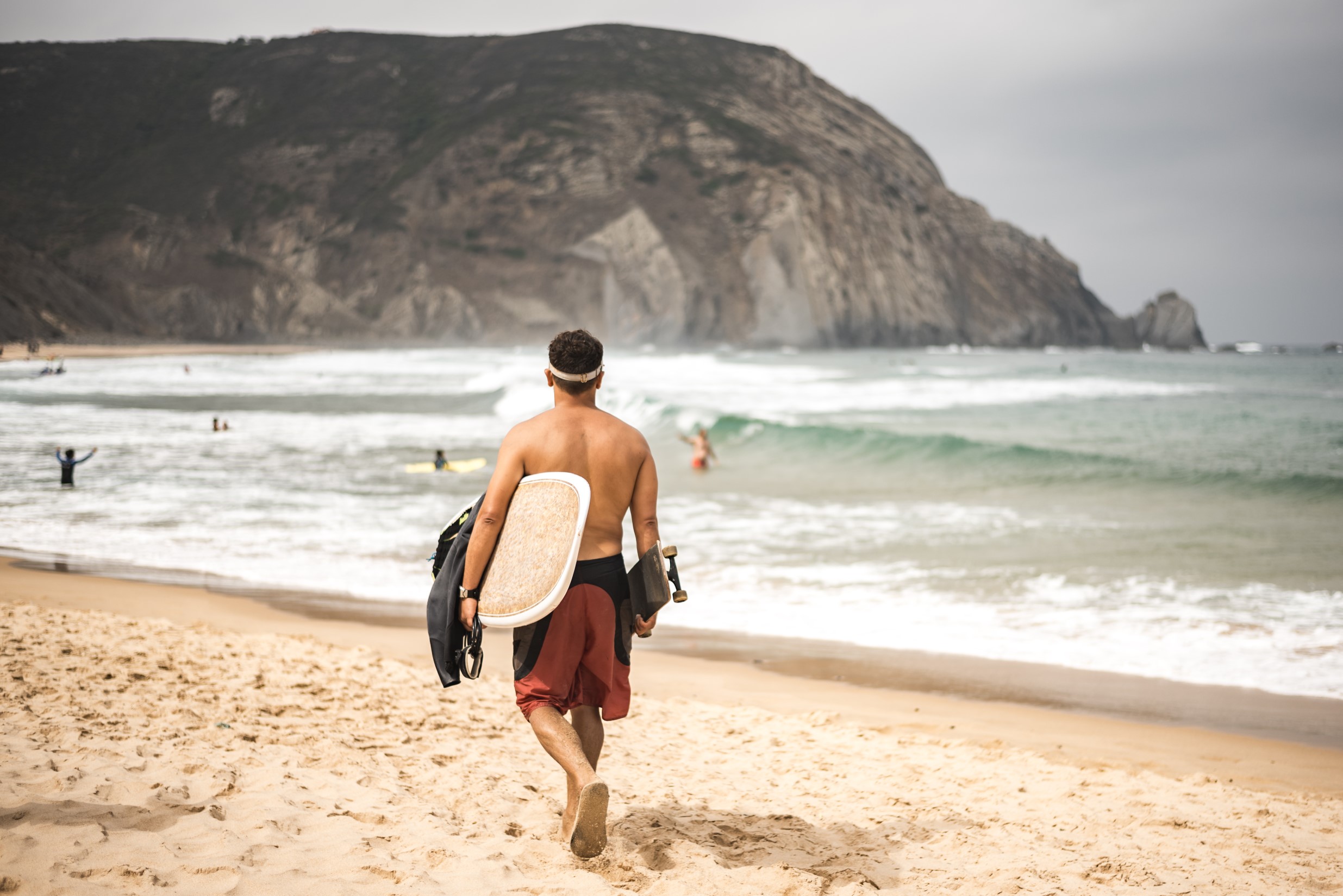 surfer walking along the beach, with surfboard and skateboard