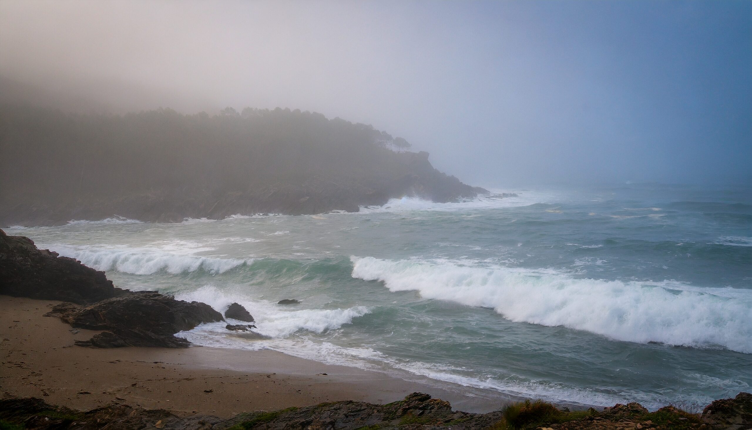 waves crashing on a beach on a foggy day.