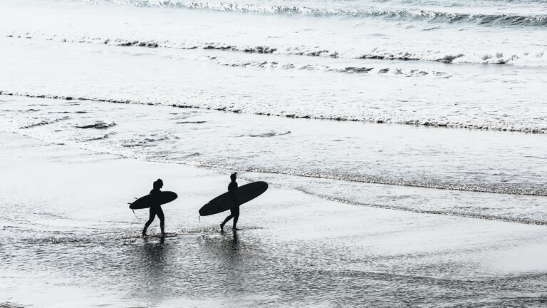 a couple of people carrying surfboards walking on a beach