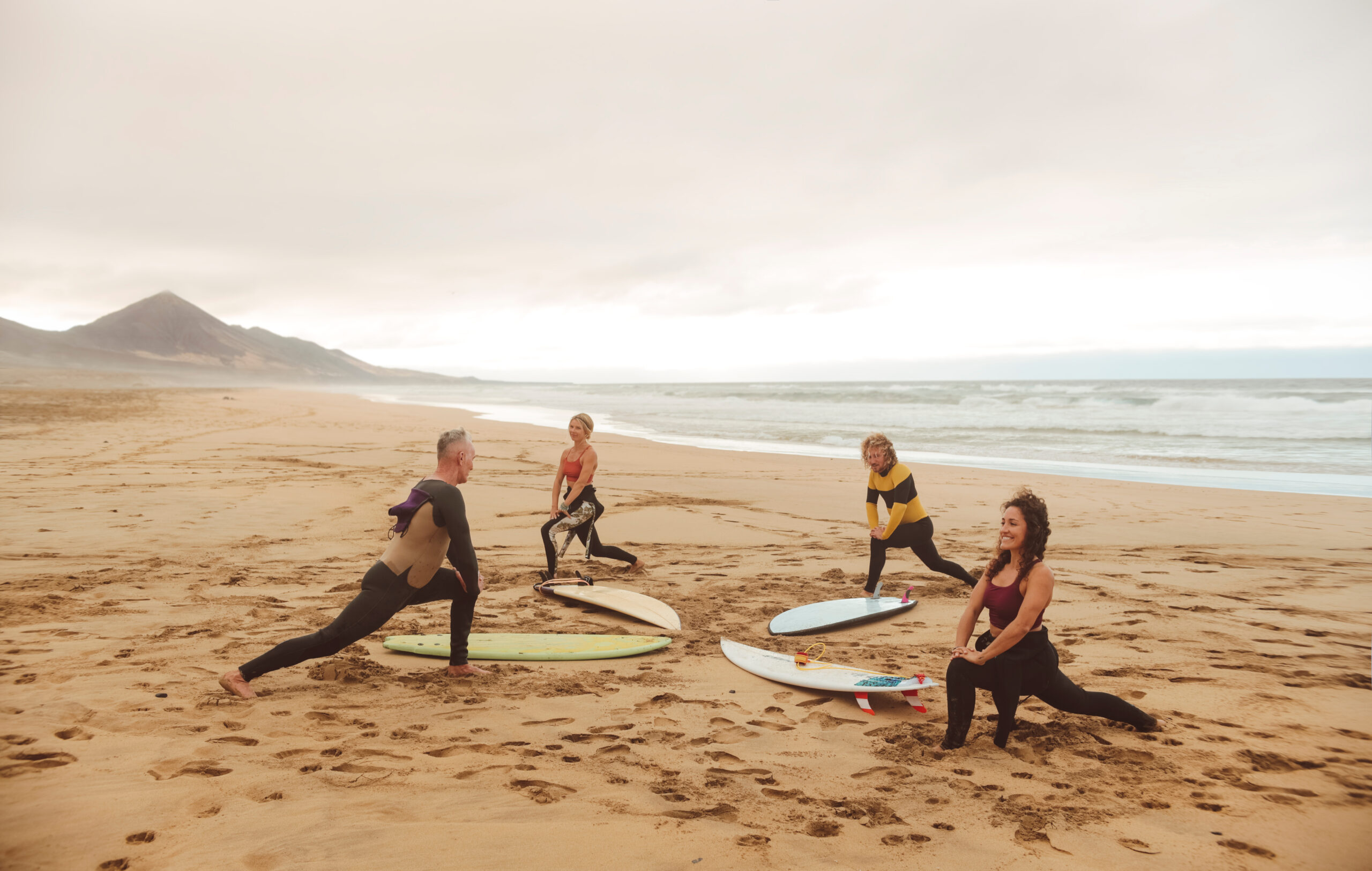 Group of people stretching at the beach, before starting a surf session. - Sportive people warming up before going in the water.