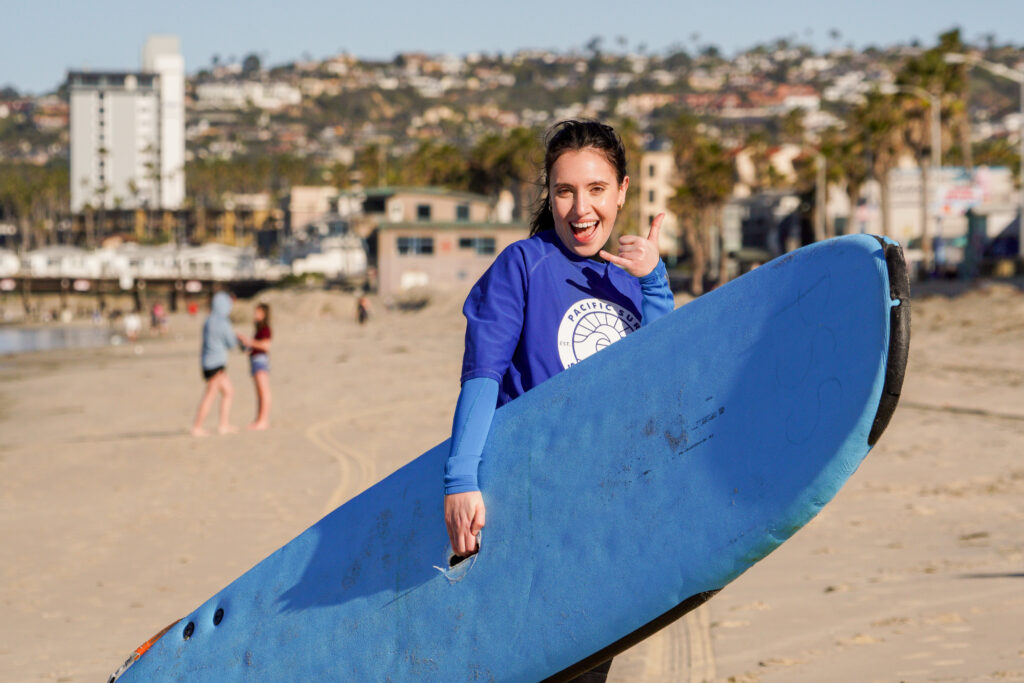 Woman holding her surfboard, happy after a surf lesson